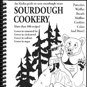 May include: Black and white illustration of a cookbook titled "Sourdough Cookery" with a bear and a man cooking pancakes. The book cover text includes "True Alaska Gold!" and "Bear Approved!"