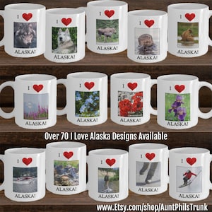 May include: A collection of 10 white ceramic mugs with red hearts and various images of Alaska. The mugs feature images of a wolf, a dog, a moose, an otter, a bear, flowers, a plane, a landscape, a person fishing, ice skates, and a skier. The text "I Love Alaska!" is printed on each mug. Over 70 I Love Alaska Designs Available. www.Etsy.com/shop/AuntPhilsTrunk