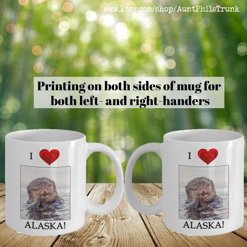 May include: White ceramic mug with a red heart and the text "I  ALASKA!" printed on it. The mug features a photo of a sea otter in the water. The mug is printed on both sides.