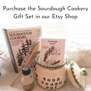 May include: A sourdough cookery gift set featuring a spiral-bound cookbook, a small booklet, a ceramic sourdough pot, a wooden spoon, and a small bottle. The pot is cream-colored with the words "SOUR DOUGH POT" and a green rim. The text "Purchase the Sourdough Cookery Gift Set in our Etsy Shop" is at the top.