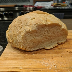 May include: A freshly baked loaf of white bread, sliced open to reveal the soft, fluffy interior. The bread is sitting on a wooden cutting board.