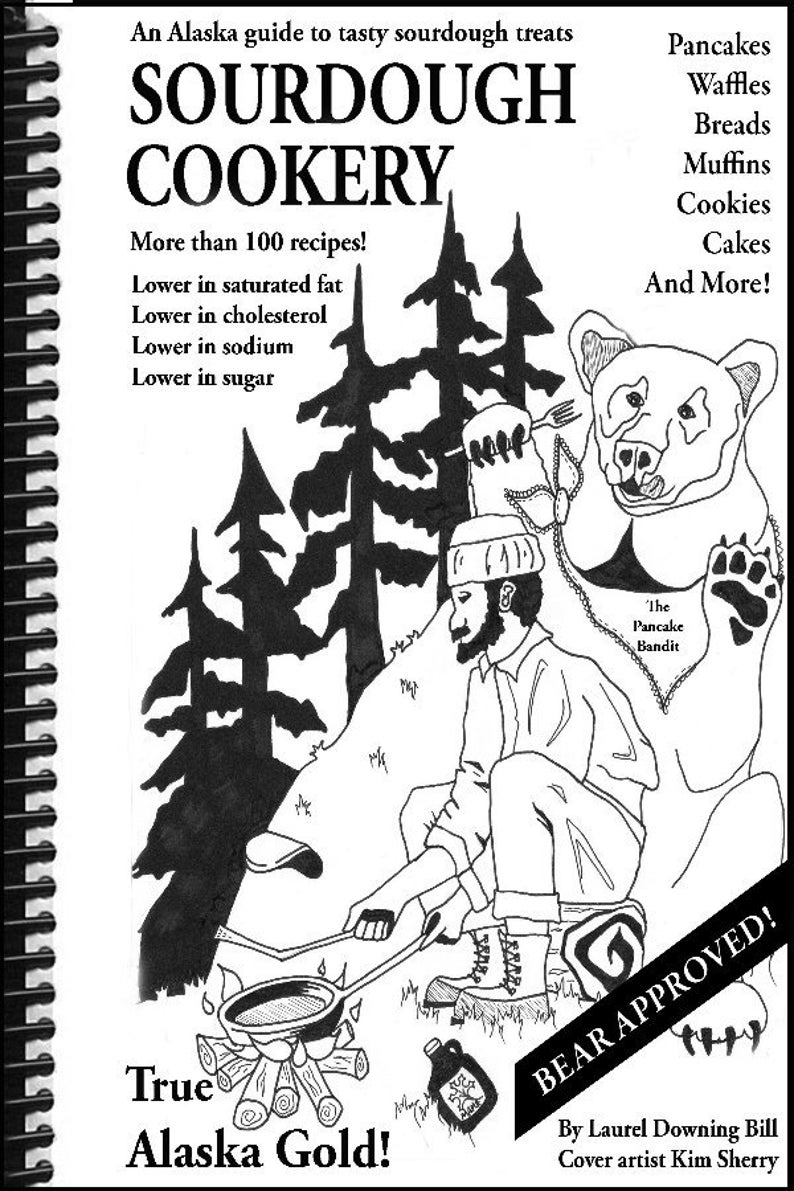 May include: Black and white illustration of a cookbook titled "Sourdough Cookery" with a bear and a man cooking pancakes. The book cover text includes "True Alaska Gold!" and "Bear Approved!"