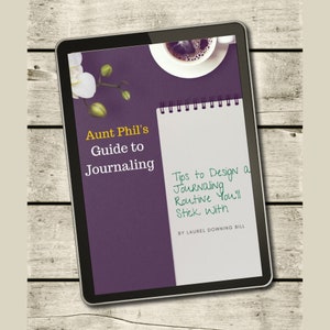May include: A digital tablet displaying a purple background with the text "Aunt Phil's Guide to Journaling" and a white notebook with the text "Tips to Design a Journaling Routine You'll Stick With" written in green ink. The text "BY LAUREL DOWNING BILL" is also visible on the notebook.