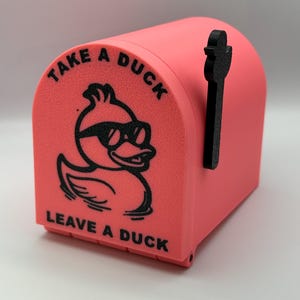 May include: A coral-colored mailbox with a black handle and a duck graphic wearing sunglasses. The text "TAKE A DUCK" and "LEAVE A DUCK" are printed above and below the duck illustration.