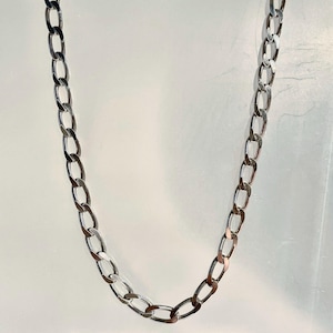May include: A silver-colored curb chain necklace. The chain is composed of interlocking oval links, creating a classic and versatile design. The necklace is displayed against a plain white background, highlighting its polished finish and simple elegance.