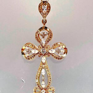 May include: Gold-toned pendant necklace featuring a cross design. The cross is adorned with clear and amber-colored gemstones. The necklace has a delicate chain and a decorative top element.