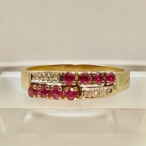 May include: A gold ring featuring two rows of vibrant red gemstones, likely rubies, interspersed with smaller, clear gemstones. The ring has a classic design with a polished gold band, showcasing the gemstones' rich color.