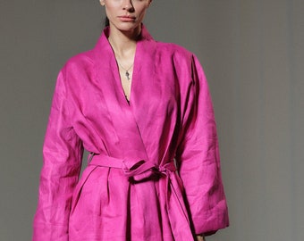May include: A woman is wearing a pink linen pantsuit with a wide belt. The pants are wide-legged and the jacket has long sleeves and a relaxed fit.