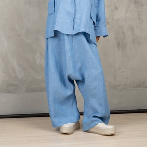 May include: A light blue linen outfit, consisting of a button-down shirt with large pockets and wide-leg pants. The outfit is paired with white platform shoes. The clothing is made of a soft, flowing fabric.
