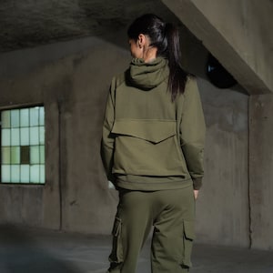 Könnte beinhalten: Ein grüner Kapuzenpullover und eine passende Cargohose. Der Pullover hat eine große Tasche auf der Rückseite. Die Hose hat mehrere Taschen an den Beinen.