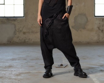 Puede incluir: Una mujer con un top negro transparente sin mangas y pantalones negros de corte holgado y fluido. Está de pie en una habitación con paredes de hormigón y ventanas.