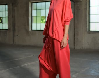 May include: A woman wearing a coral colored, loose-fitting top and pants. The outfit is made of a soft, flowing fabric. She is wearing gray sneakers.
