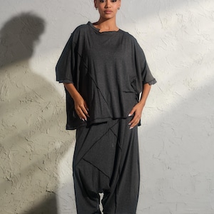 May include: A dark gray two-piece outfit featuring a loose-fitting top and wide-leg pants. The top has short sleeves and a round neckline. The pants have a unique, asymmetrical design. The outfit is paired with black platform boots.