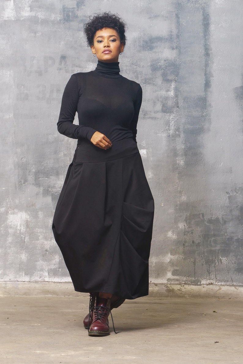 May include: A woman wearing a black turtleneck sweater and a black, flowing skirt. She is wearing burgundy ankle boots.
