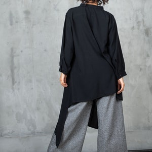 May include: A black long-sleeved shirt with a high collar and a high-low hemline. The shirt is paired with gray wide-leg pants.