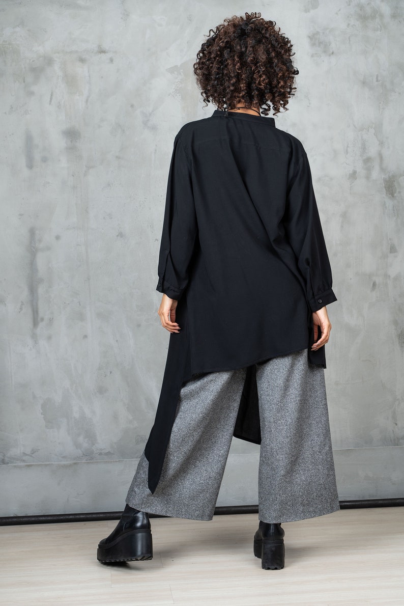 May include: A black long-sleeved shirt with a high collar and a high-low hemline. The shirt is paired with gray wide-leg pants.