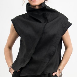 May include: A black linen shirt with a high, folded collar and short sleeves. The shirt is draped in a loose, asymmetrical style.