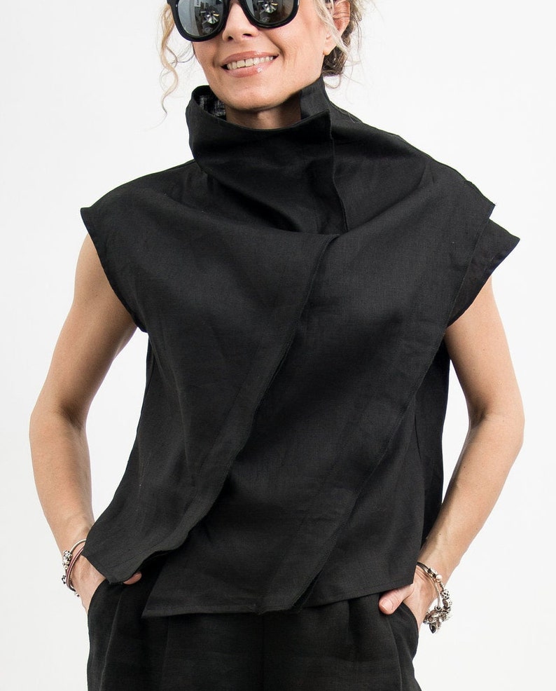 May include: A black linen shirt with a high, folded collar and short sleeves. The shirt is draped in a loose, asymmetrical style.