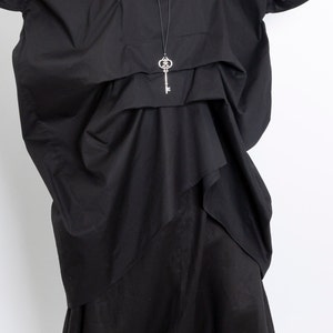 May include: A black, oversized shirt with a key-shaped pendant necklace. The shirt has a loose, flowing fit and is made of a soft, comfortable fabric.