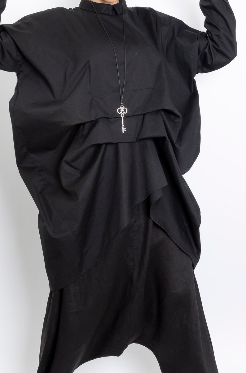 May include: A black, oversized shirt with a key-shaped pendant necklace. The shirt has a loose, flowing fit and is made of a soft, comfortable fabric.