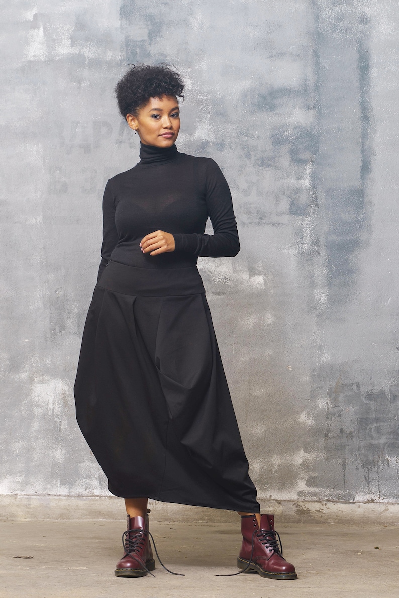May include: A woman wearing a black turtleneck top and a black, flowing skirt. She is wearing burgundy leather boots with laces.