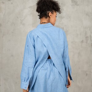 May include: A light blue linen shirt dress with a criss-cross back detail. The dress has long sleeves and a collared neckline.