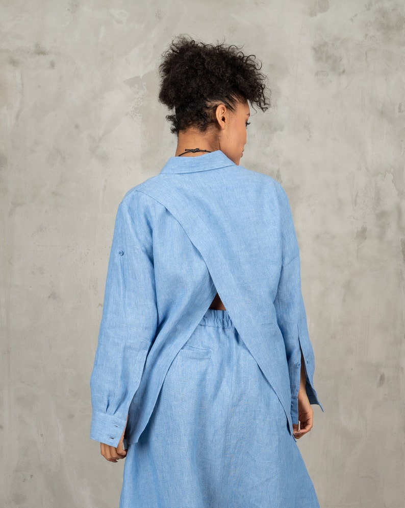 May include: A light blue linen shirt dress with a criss-cross back detail. The dress has long sleeves and a collared neckline.