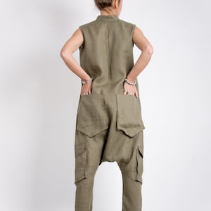 May include: A khaki linen jumpsuit with large cargo pockets and a cuffed hem. The jumpsuit has a sleeveless design and a high neckline.