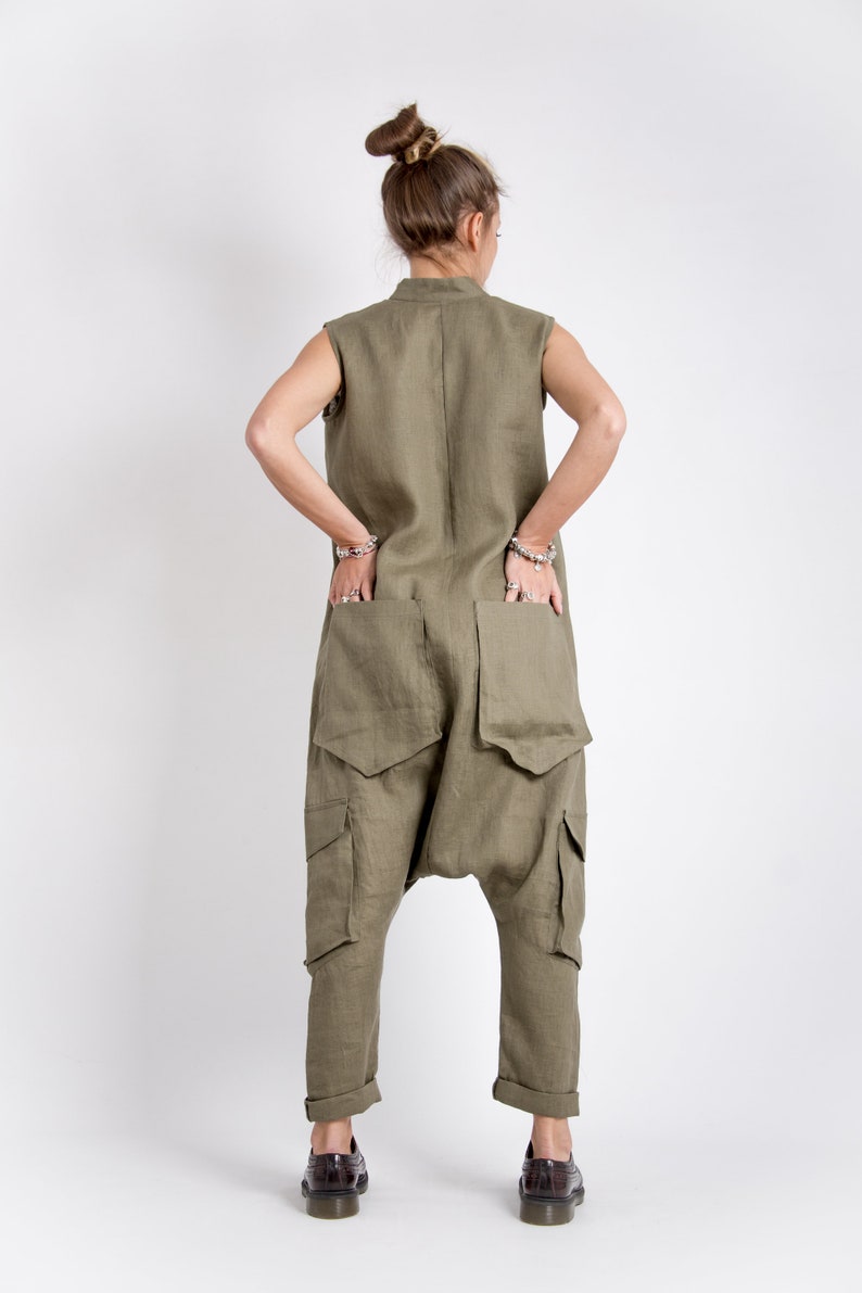 May include: A khaki linen jumpsuit with large cargo pockets and a cuffed hem. The jumpsuit has a sleeveless design and a high neckline.