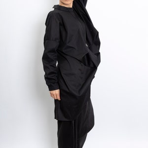 May include: A black long-sleeved shirt with a draped design and a black skirt. The person is wearing black sandals with white soles.