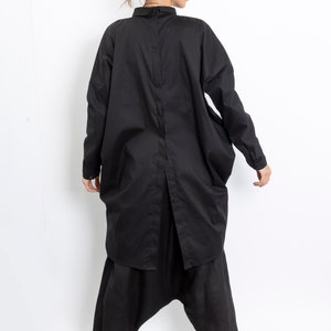 May include: A black long-sleeved shirt with a button-up front and a loose, oversized fit. The shirt is worn with black pants and a black hat.