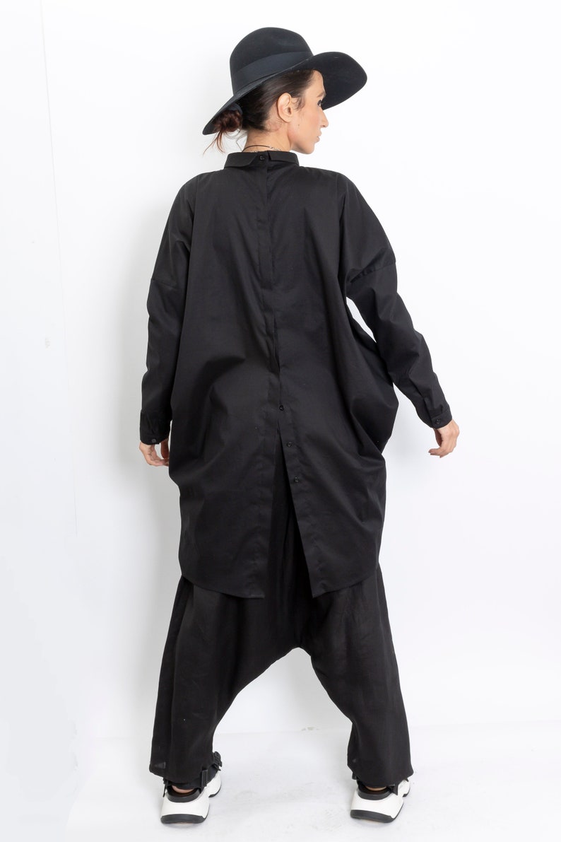 May include: A black long-sleeved shirt with a button-up front and a loose, oversized fit. The shirt is worn with black pants and a black hat.