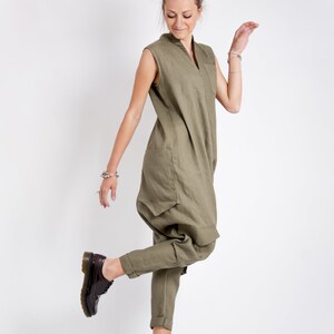 May include: A woman wearing a green linen jumpsuit with a v-neck and pockets. She is wearing brown leather lace-up shoes.
