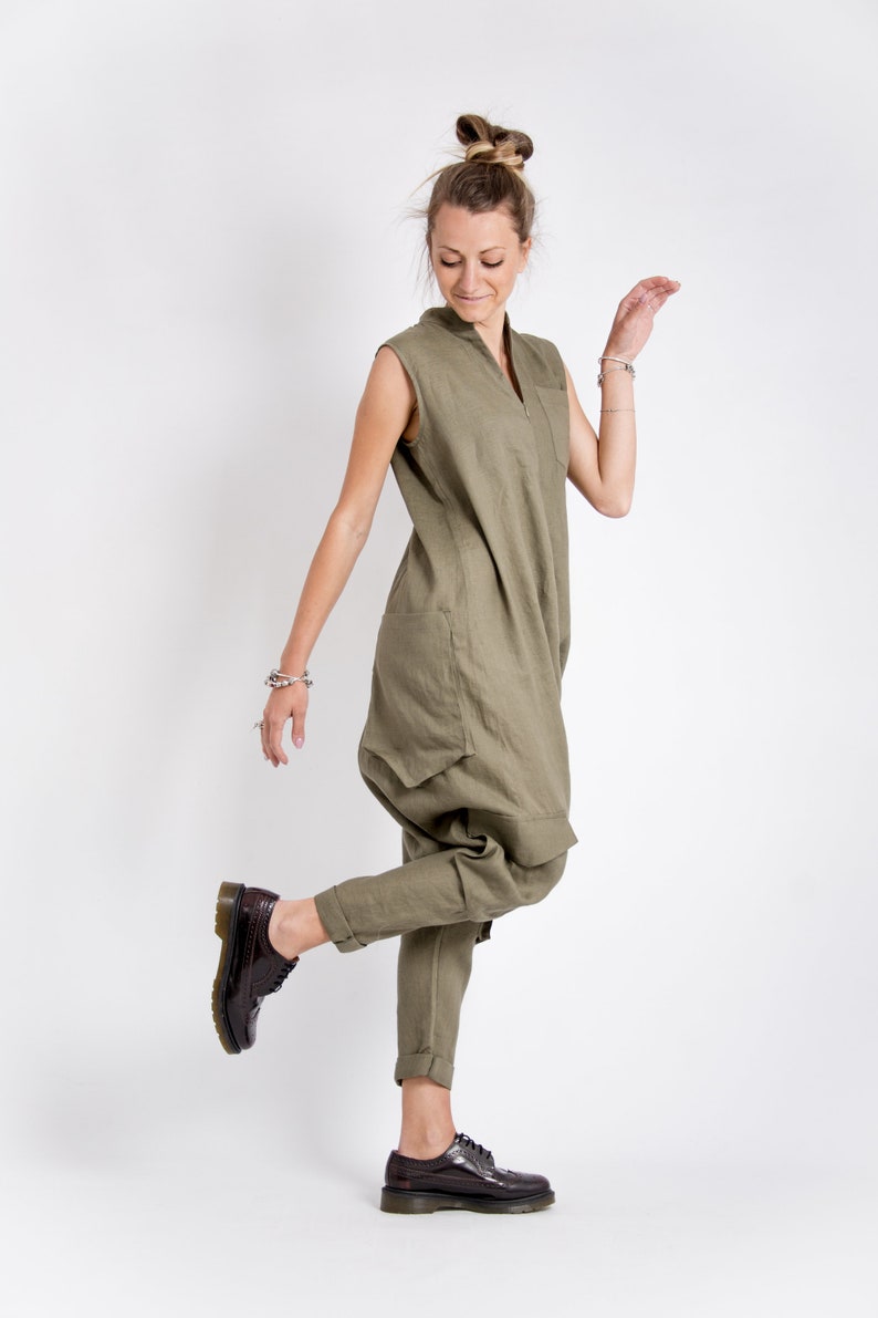 May include: A woman wearing a green linen jumpsuit with a v-neck and pockets. She is wearing brown leather lace-up shoes.