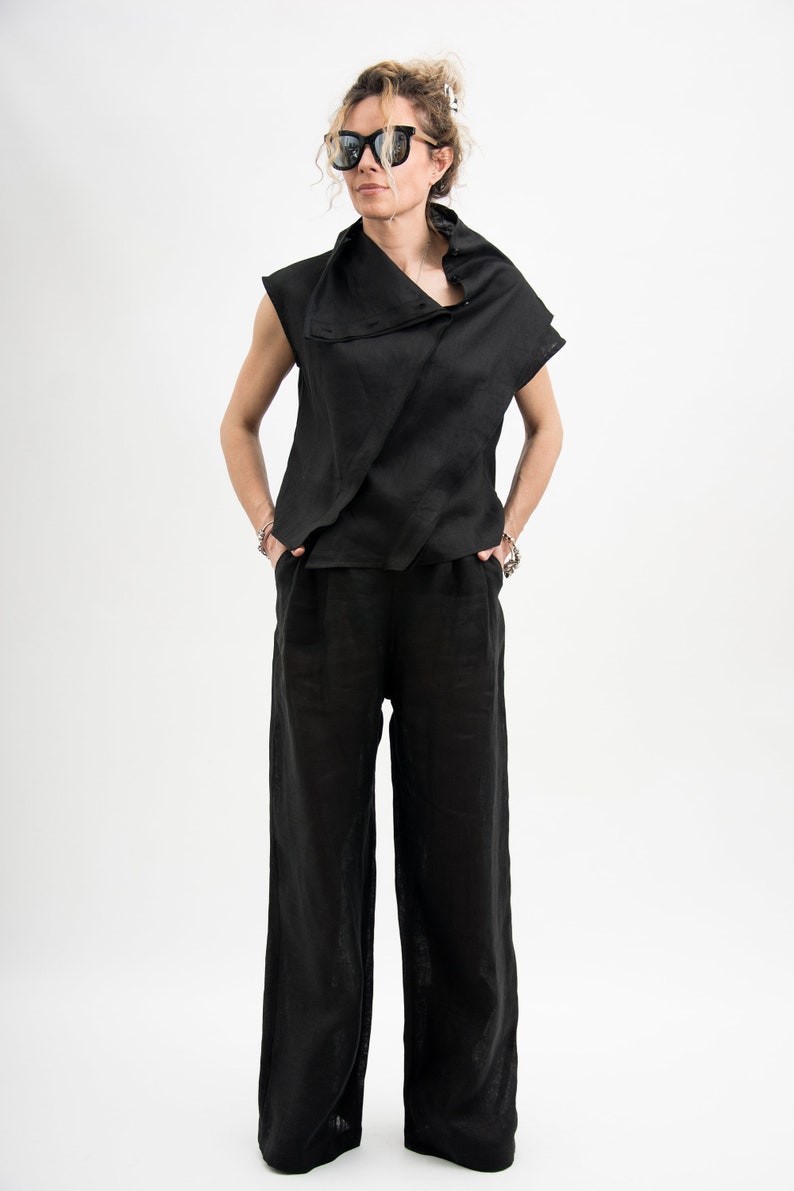 May include: A black sleeveless top with a draped neckline and a matching pair of wide-leg pants. The outfit is made of a lightweight fabric and has a relaxed fit.