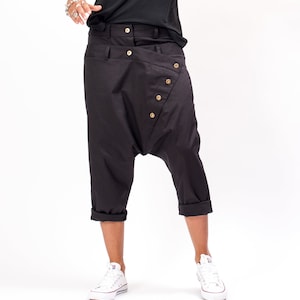 Pode incluir: Calça preta com um design único que apresenta uma costura diagonal e vários botões. A calça é cropped e tem um caimento solto e confortável.
