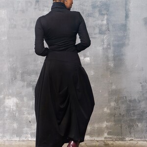 May include: A woman wearing a black turtleneck top and a black, flowing skirt. She is wearing burgundy leather boots with laces.