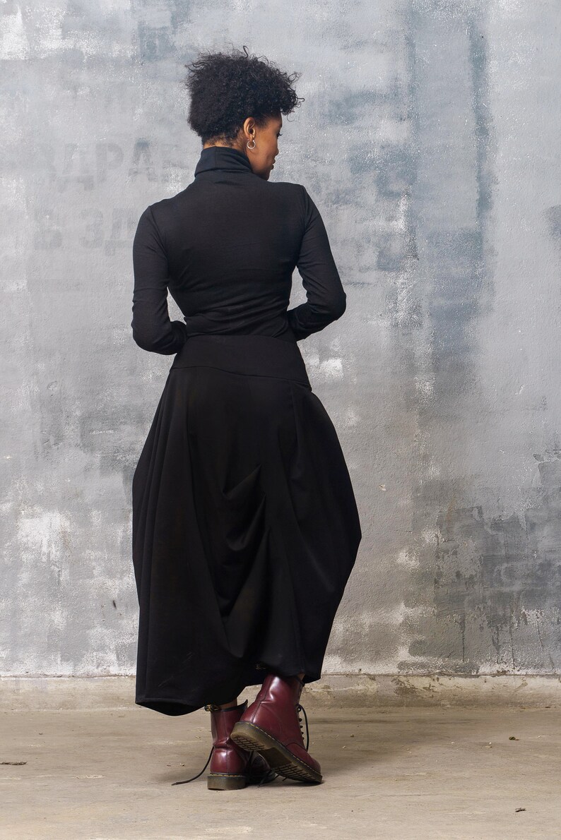 May include: A woman wearing a black turtleneck top and a black, flowing skirt. She is wearing burgundy leather boots with laces.