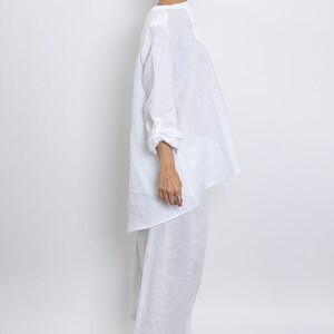 May include: A white linen outfit, consisting of a long-sleeved top and wide-leg pants. The top has a relaxed fit with rolled-up sleeves. The pants are floor-length. The outfit is made of a lightweight, breathable fabric, perfect for warm weather.