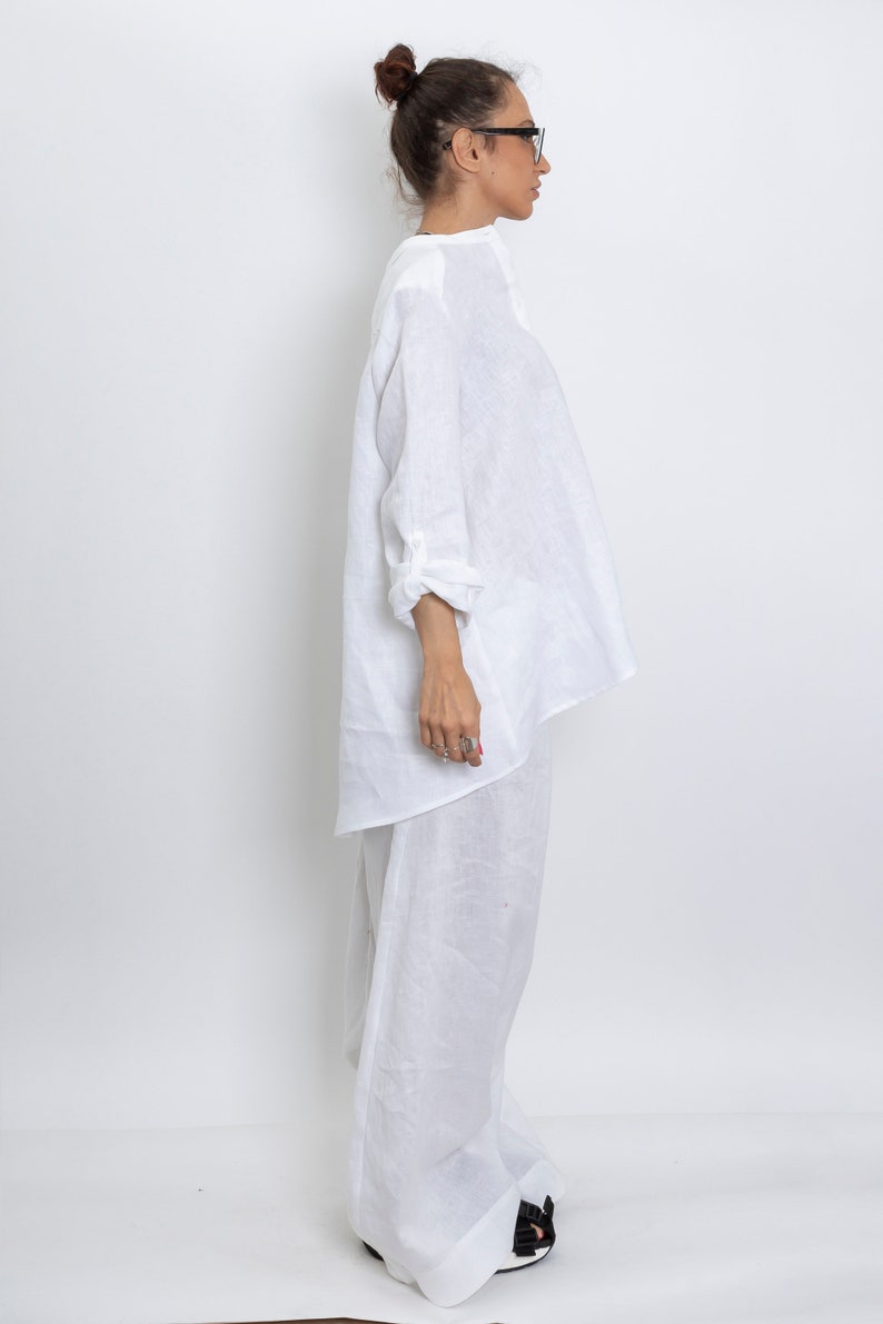 May include: A white linen outfit, consisting of a long-sleeved top and wide-leg pants. The top has a relaxed fit with rolled-up sleeves. The pants are floor-length. The outfit is made of a lightweight, breathable fabric, perfect for warm weather.