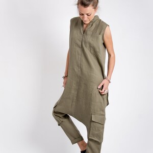 May include: A woman wearing a green linen jumpsuit with a zipper down the front and cargo pockets. She is wearing brown leather shoes.
