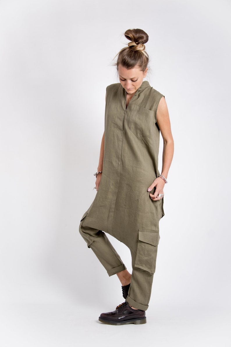 May include: A woman wearing a green linen jumpsuit with a zipper down the front and cargo pockets. She is wearing brown leather shoes.