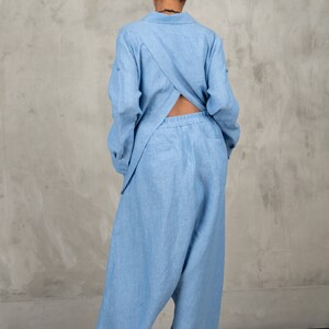 May include: A light blue linen jumpsuit with a criss-cross back detail. The jumpsuit has a relaxed fit and wide legs.