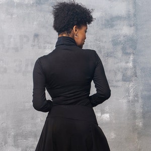 May include: A woman wearing a black turtleneck top and a black skirt. The skirt is gathered at the waist and falls to the floor.