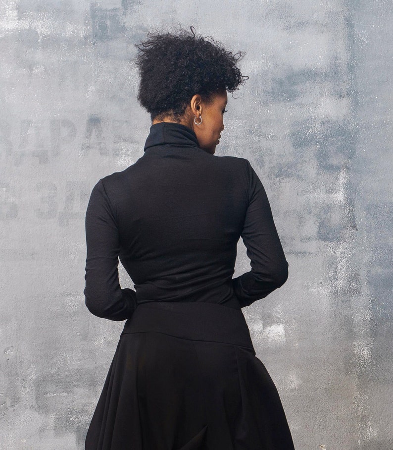 May include: A woman wearing a black turtleneck top and a black skirt. The skirt is gathered at the waist and falls to the floor.
