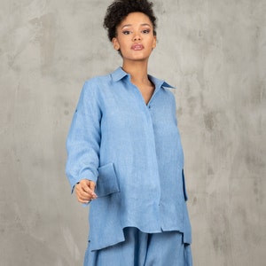 May include: A light blue linen shirt with long sleeves and a button-up front. The shirt has two large pockets on the front and a relaxed fit.