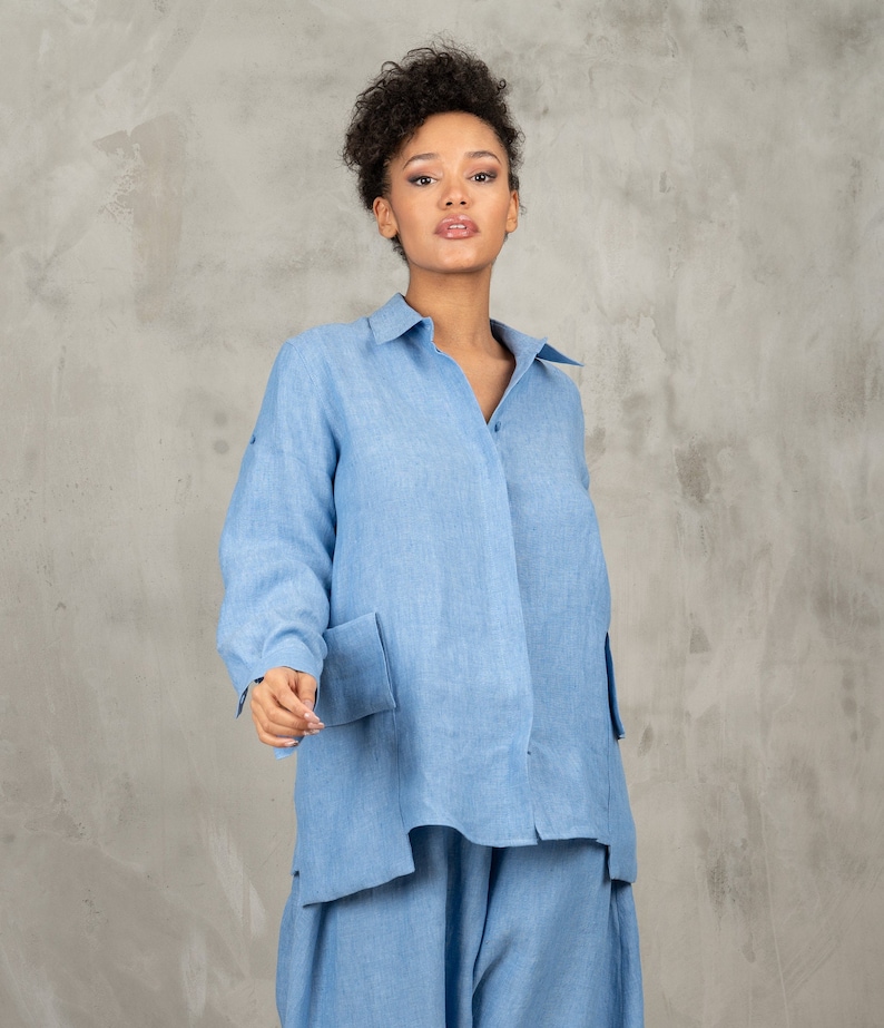 May include: A light blue linen shirt with long sleeves and a button-up front. The shirt has two large pockets on the front and a relaxed fit.