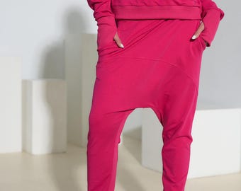 May include: A bright fuchsia long-sleeve hooded sweatshirt with a front kangaroo pocket and matching drop-crotch pants featuring side pockets. The outfit is paired with black platform sneakers with thick soles and black laces.