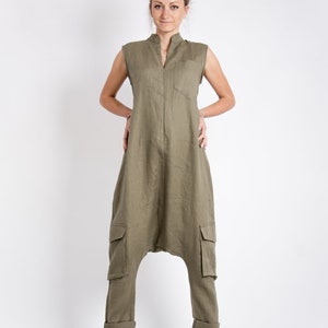 May include: A woman wearing a green linen jumpsuit with a zipper down the front and cargo pockets. She is wearing brown leather shoes.
