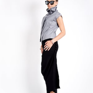 May include: A woman wearing a gray sleeveless top with a high collar and a black skirt. She is wearing black sunglasses and black shoes.